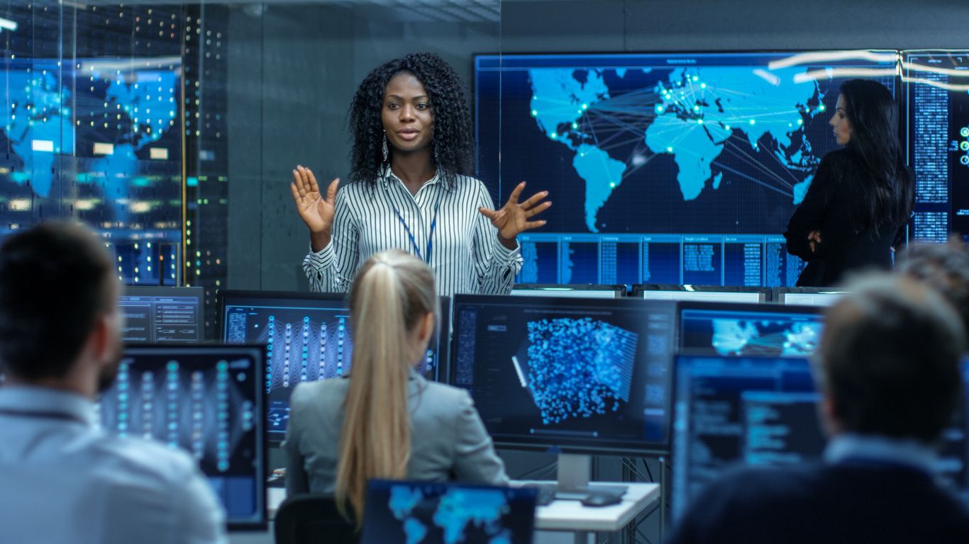 A woman standing in front of multiple monitors.